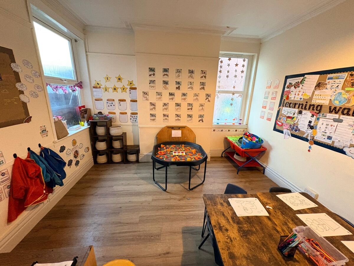 A bright playroom with tables, a sand tray and display boards